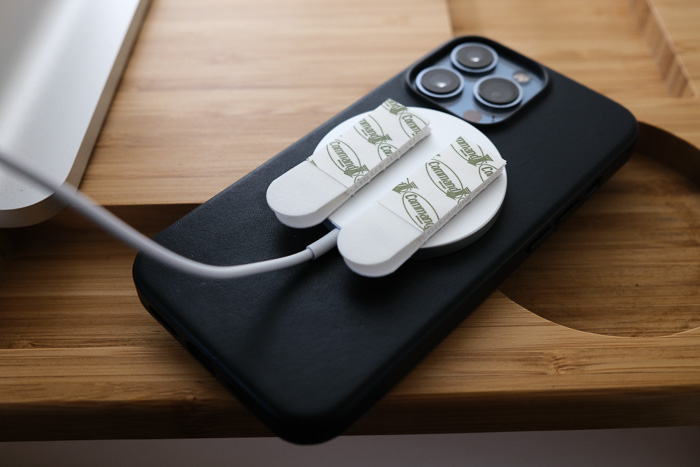 An iPhone 13 and a MagSafe charger with 3M Command Strip picture hangers stuck to MagSafe charger